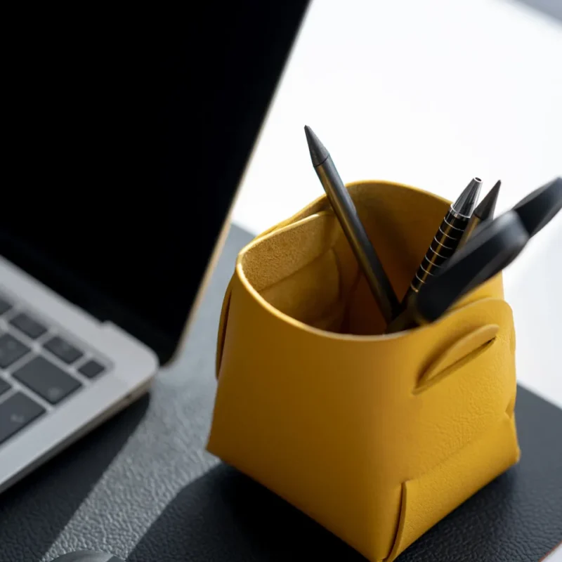 Yellow foldable leather holder containing pens on a desk