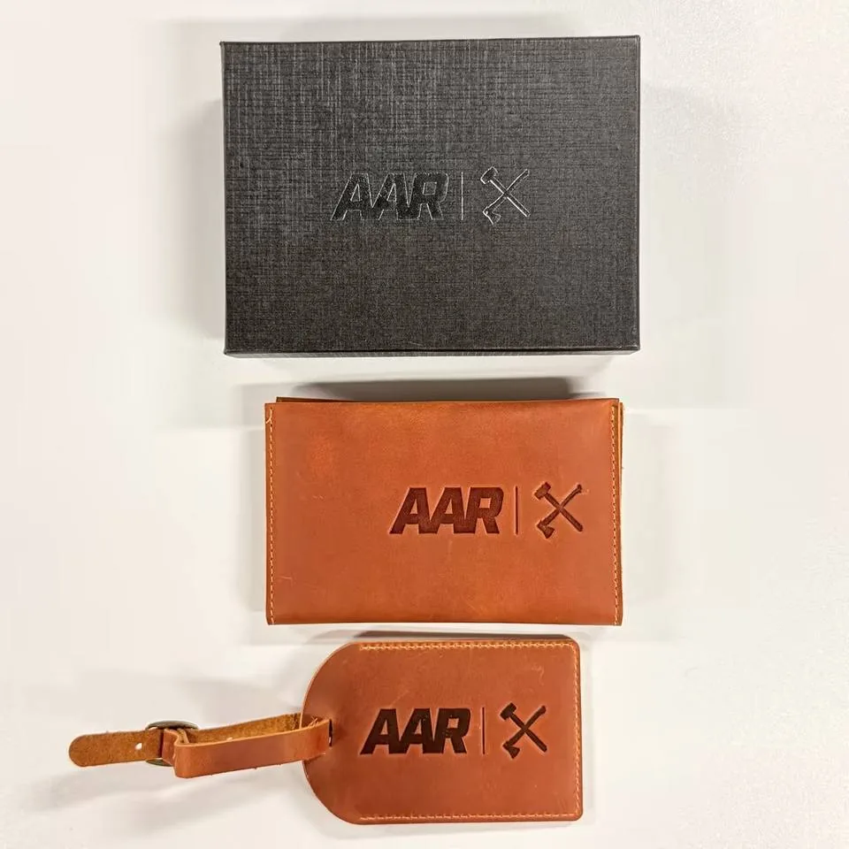 Flat lay of a black gift box, brown leather passport cover and matching luggage tag
